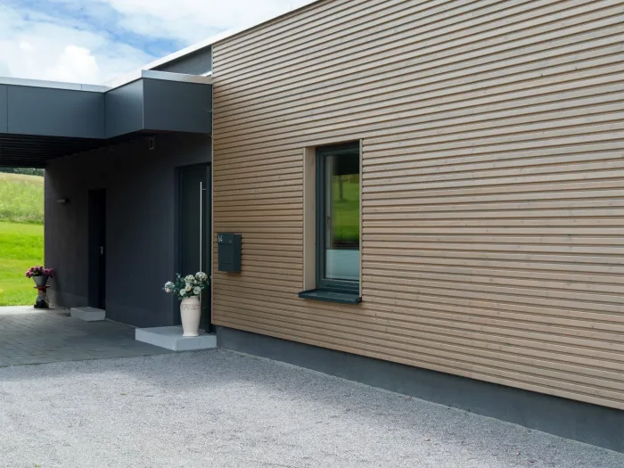 Hauseingang eines Holzhauses mit Holzfassade und dunklem Vordach
