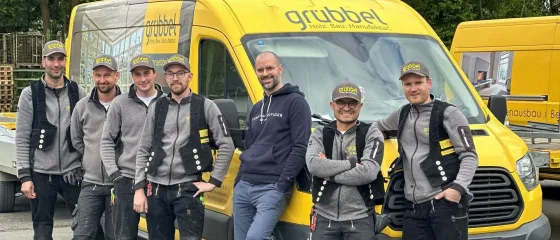 Mitarbeiter vor einem gelben Grübbel-Firmenwagen