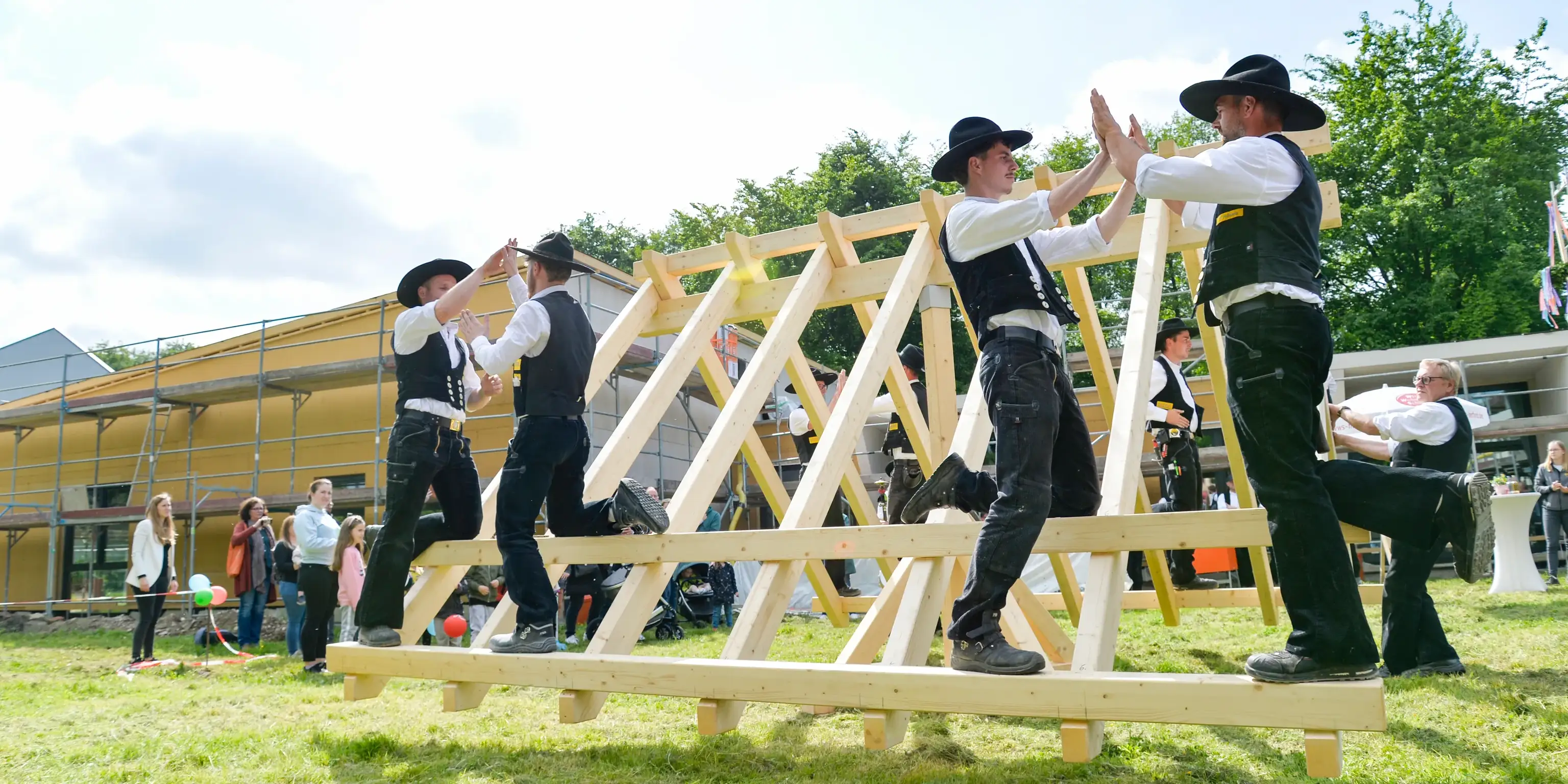 Zimmerer in Kluft klatschen sich auf einem Holzgerüst ab, Fest bei Grübbel in Bad Oeynhausen