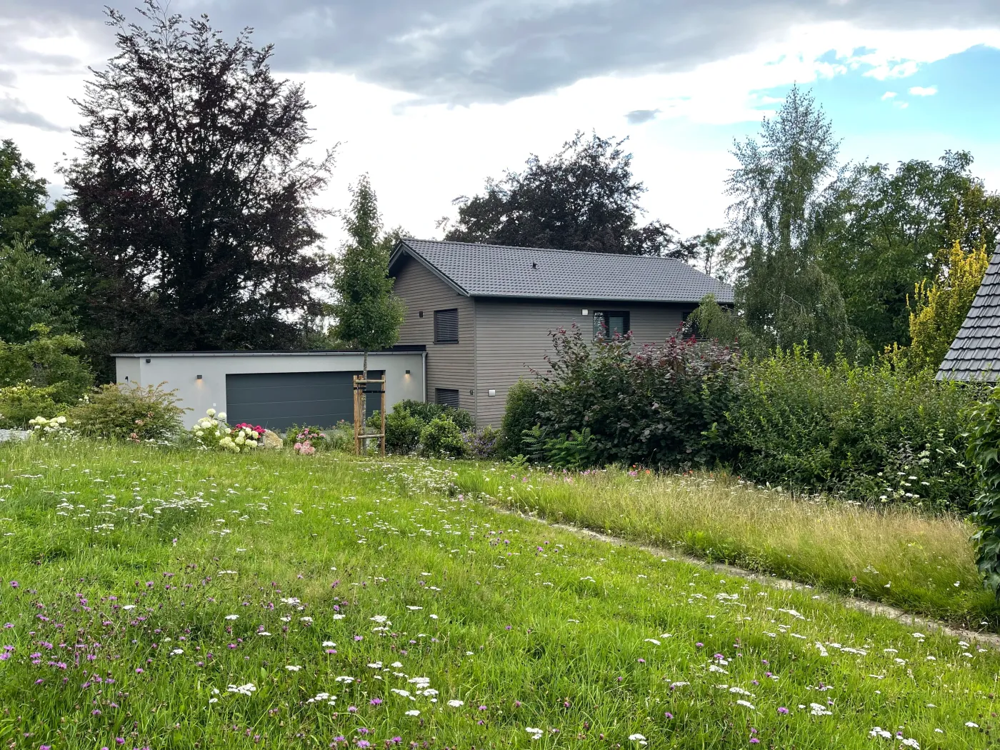 Einfamilienhaus in Bad Oeynhausen: Wohnhaus mit Holzfassade hinter einer Blumenwiese