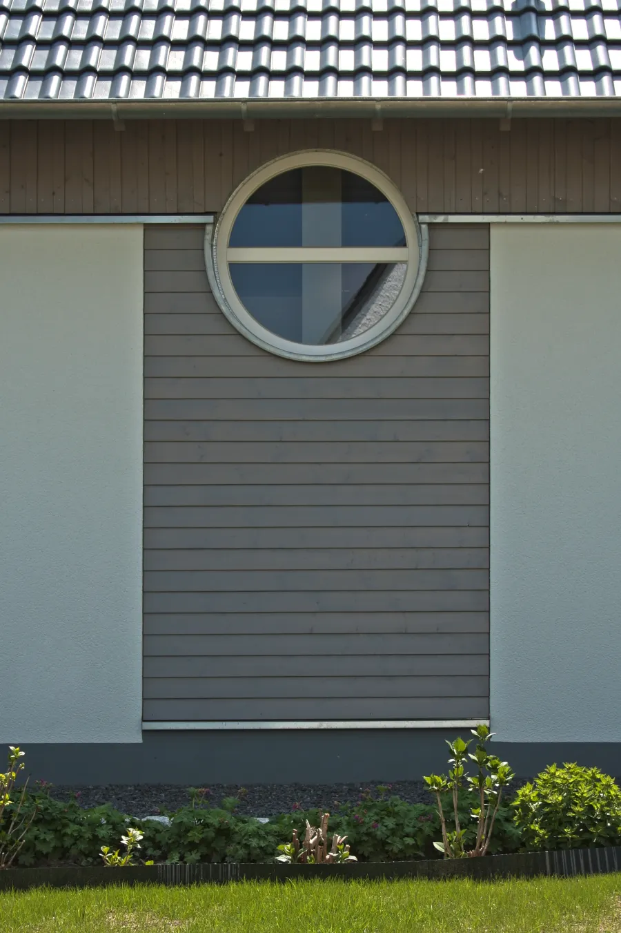 Einfamilienhaus in Holzhausen: Rundfenster in grauer Holzverschalung