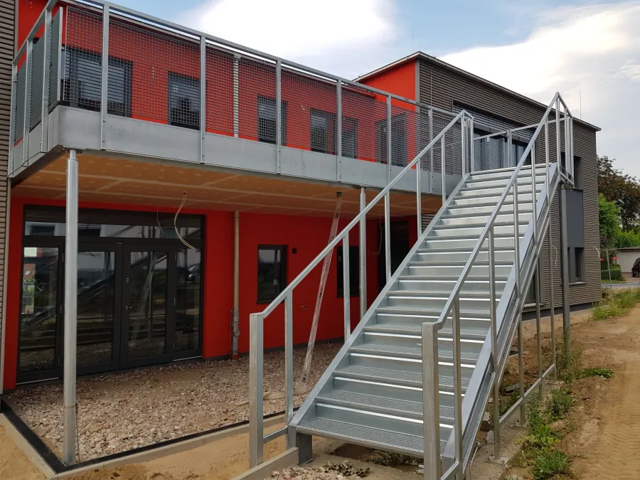 Soziale Wohnanlage in Spenge: Außentreppe und Laubengang an roter Fassade