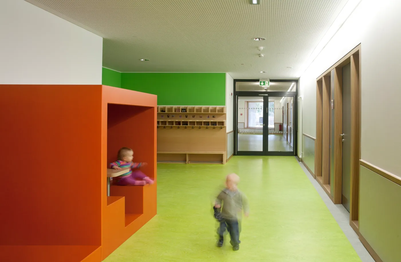 Kita in Holzrahmenbauweise in Hannover: Flur mit orangefarbener Spielnische und Kind
