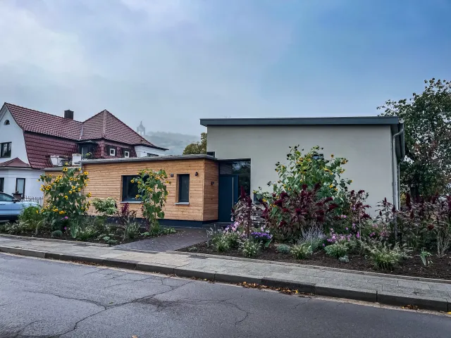 Portrait Zuhause in der Obstwiese: Bungalow mit Holzanbau hinter blühendem Vorgarten