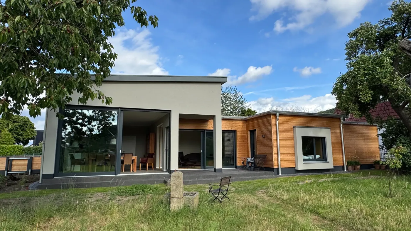 Portrait Zuhause in der Obstwiese: Bungalow mit großer Verglasung und Terrasse im Garten